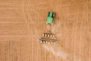 Aerial view of a tractor tilling a dusty field showing the connection between products and results in our every day.