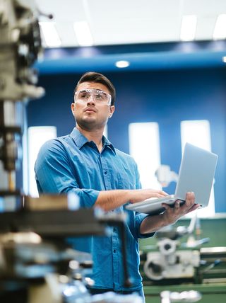 Research engineer testing equipment with a laptop in a manufacturing facility.