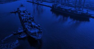 Aerial view of a container ship carrying cargo in a port with a blue color filter over top.