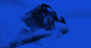 Super ATV riding over a dune in the desert sand with a blue filter over top.