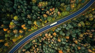 Aerial view of truck driving through a green forest.