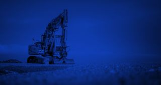 Excavator at a construction site with blue sky behind and blue color filter over top.